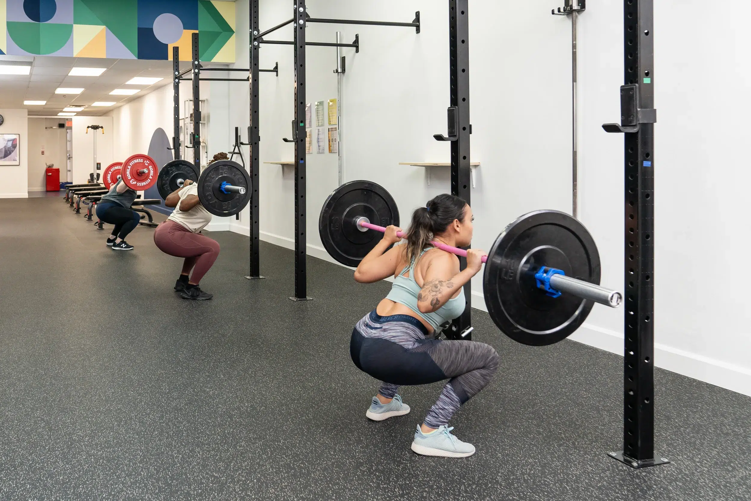 Three people doing a barbell squat exercise in a group fitness class.