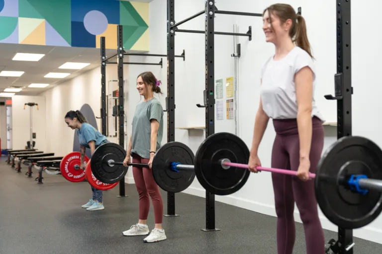 Three smiling women doing a deadlift in a group fitness class.