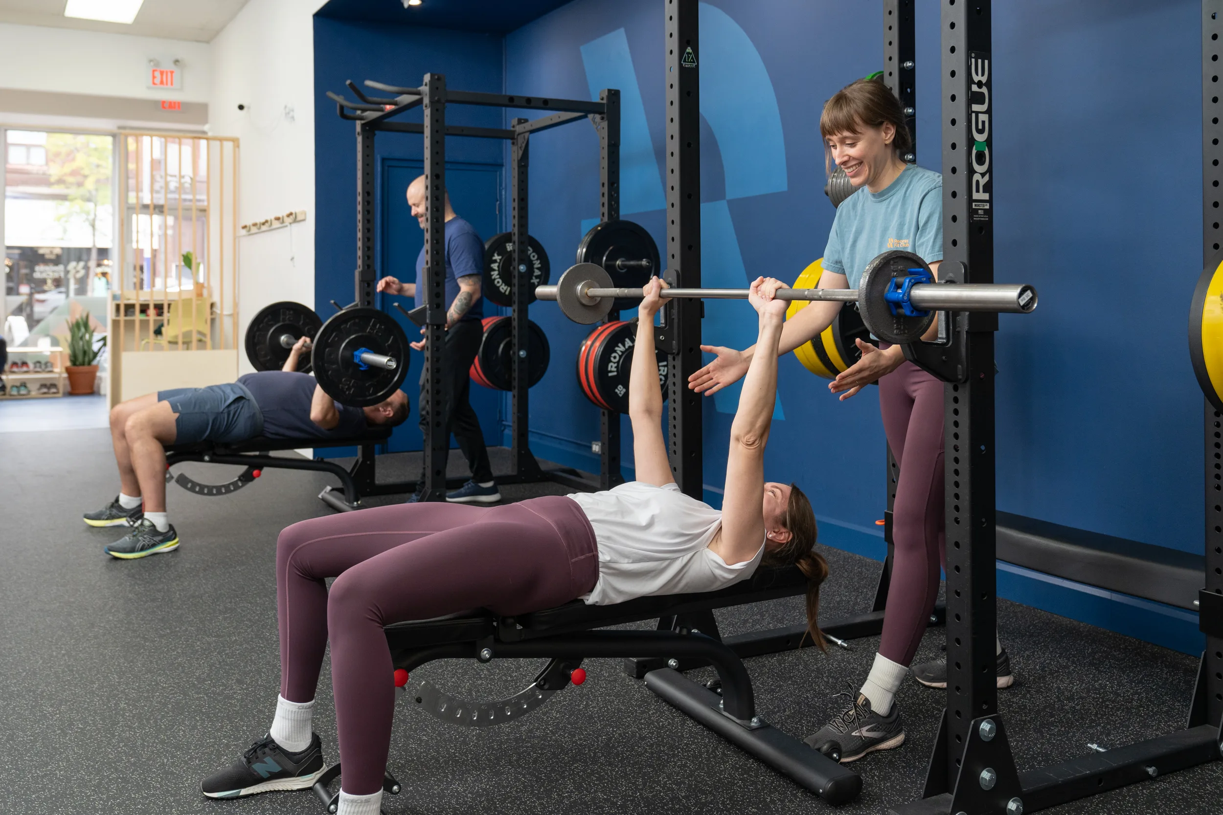Two people in the gym doing a barbell exercise with two personal trainers.