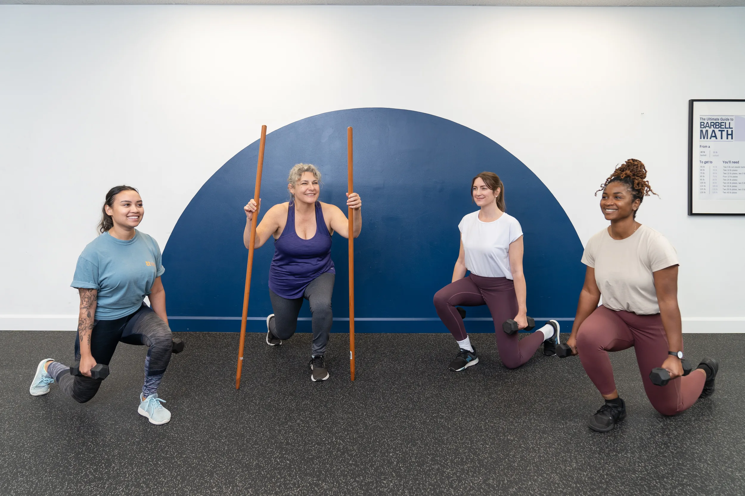 Group fitness class - split squat. Four women performing a split squat smilling.