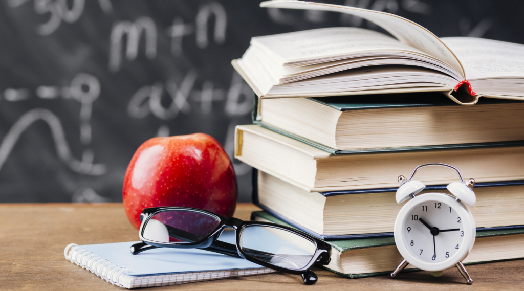 Image of a teachers desk with apple and books in a pile