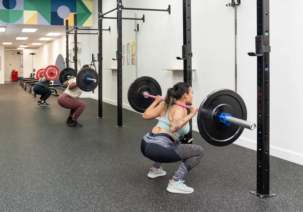 Three people doing a barbell squat exercise in a group fitness class.