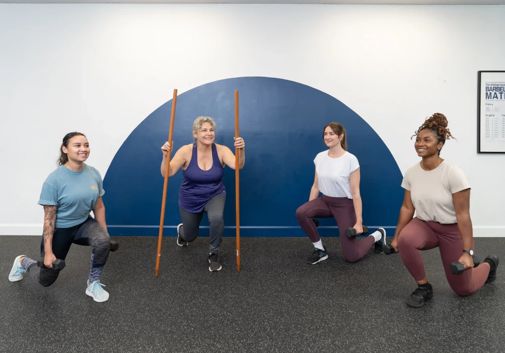 Group fitness class - split squat. Four women performing a split squat smilling.