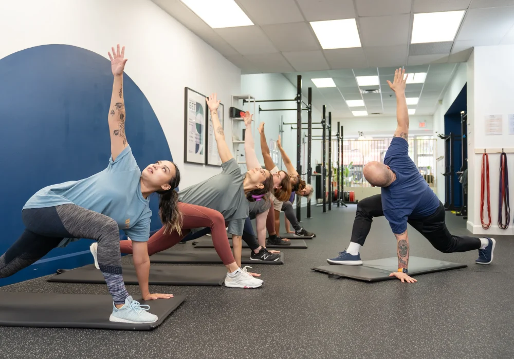 Group fitness class performing a mobility exercise in a bright gym